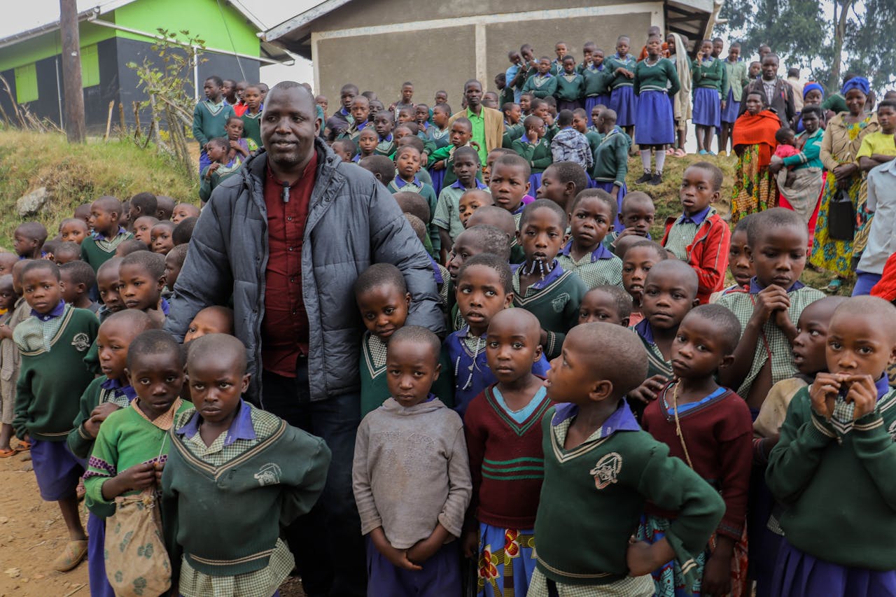 A large group of African children and an adult gather outside a rural school setting, showcasing community spirit.
